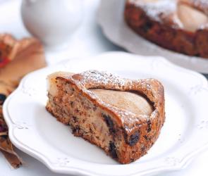 Ein Birnen-Walnusskuchen vor einem weißen Hintergrund, mit Puderzucker bestreut