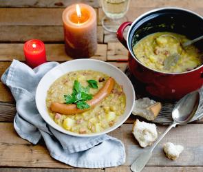 Deftige Erbsensuppe mit Wiener Würstchen in einem Teller, daneben der Suppentopf.