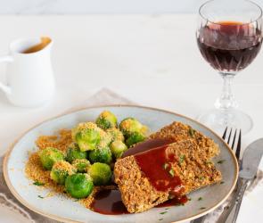 Deftiger Nussbraten mit Rosenkohl, Semmelbrösel und Sauce auf einem Teller angerichtet.