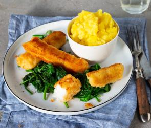 Fischstäbchen, Spinat und Kartoffelpüree auf Teller mit Wasserglas und Besteck