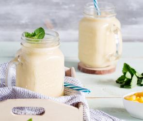Gelber Mango-Lassi mit Kokosmilch in zwei Gläsern mit Strohhalm.