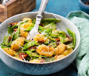 Gnocchi mit Zuckerschoten und getrockneten Tomaten in Parmesansauce in einer Schale 