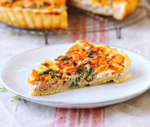 Ein Quichestück auf einem Teller vor der angeschnitten Quiche. 