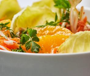Karottensalat mit Sellerie, Äpfeln und Orangenfilets in einer Schale, wird mit Dressing übergossen.