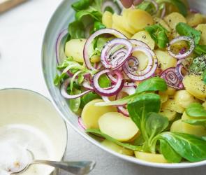 Kartoffelsalat mit Nussbutter in einer Schüssel, eine Hand streut Salz darüber.