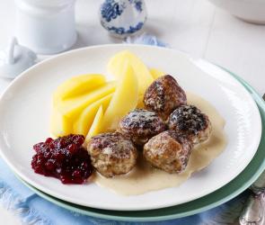 Köttbullar mit Kartoffeln, Sauce und Preiselbeeren auf einem Teller.