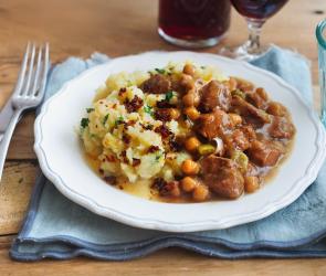 Lamgulasch mit Stampf auf einem Teller angerichtet zu einem Glas Rotwein. 