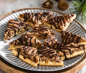 Nussecken vor winterlichem Hintergrund auf einem Teller verteilt und mit Schokolade verziert.