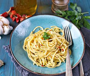 Spaghetti aglio, olio e peperoncino auf einem Teller auf einem gedeckten Tisch.