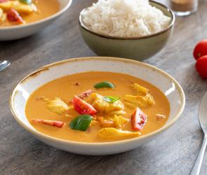 Pochierter Kabeljau mit Tomatencurry daneben Schale mit Reis.