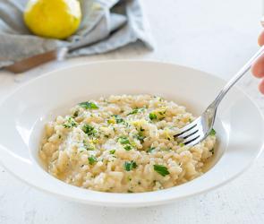Risotto mit Zitrone und Petersilie wird mit einer Gabel vom Teller genommen.