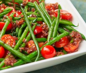 Salat von grünen Bohnen mit Balsamico-Schalotten und Kirschtomaten auf einem Teller.