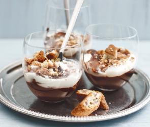 Schichtdessert mit Schokolade, Sahne und Cantuccinibroeseln in einem Glas.