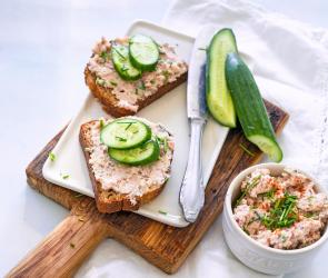 Zwei Scheiben Brot mit Streichwurst und Gurke auf Holzbrett.