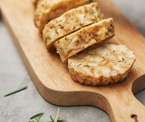 Serviettenknödel wird auf einem Holzbrett in Scheiben geschnitten.