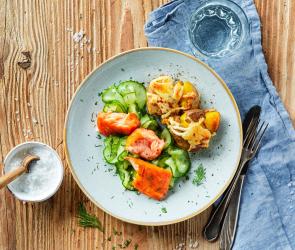 Stampfkartoffeln mit Stremellachs und Gurkensalat auf einem Teller angerichtet. 