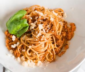 Spaghetti Bolognese auf weißem Teller garniert mit Basilikum.