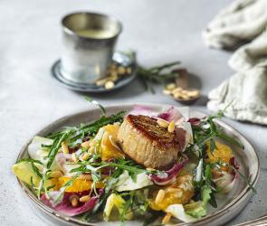 Wintersalat aus Chicorée und Orangen mit Schweinefiletmedaillons auf einem Teller.