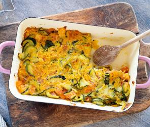 Zucchini-Tomaten-Auflauf in einer Auflauffirm auf einem Holzbrett,