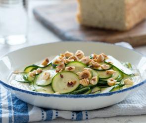 Marinierte Zucchini mit gerösteten Haselnüssen und Ricotta in einem tiefen Teller angerichtet.
