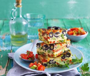 Frittata mit Tomatensalat auf einem Teller gestapelt.