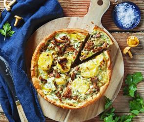 Quiche mit Kartoffeln und Pfifferlingen auf einem Holzbrett.