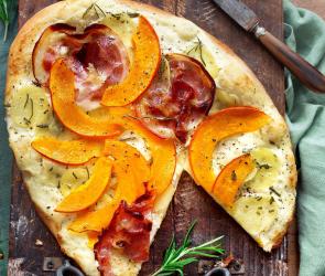 Pizza bianca mit Kürbis und Kartoffeln auf einem Holzbrett.