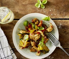 Buntes Gemüse mit Hähnchen und Basilikumblättern auf einem Teller.