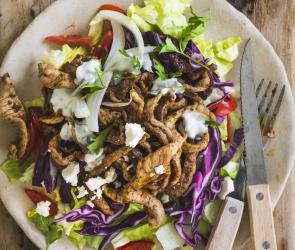Teller mit Fleisch und Salat auf Holzbrett
