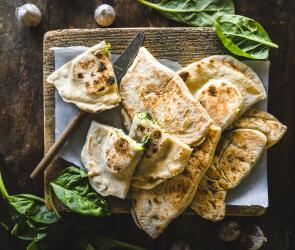 Teigfladen mit Füllung auf einem Holzbrettchen.