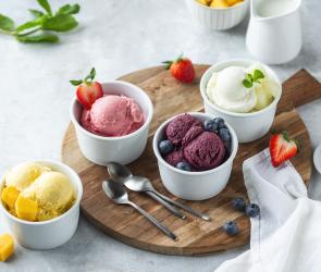 Fruchteis zu Kugeln portioniert in kleinen Schälchen, die auf einem Holzbrett stehen.