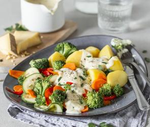 Buntes Gemüse und Kartoffeln in Käsesauce auf einem gedeckten Tisch serviert.