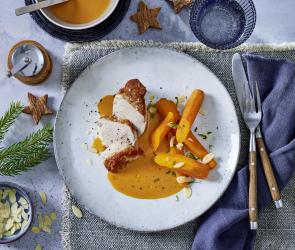 Schweinefilet mit Karotten und Rahmsauce hünsch angerichtet auf einem hellen Teller.