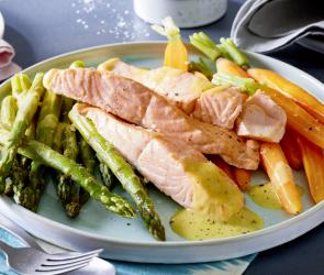 Grüner Spargel mit Lachs und Senf-Butter auf einem Teller angerichtet.