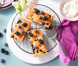 Blechkuchen mit Blaubeeren und Brombeeren in Stücke geschnitten auf einem Kuchengitter.