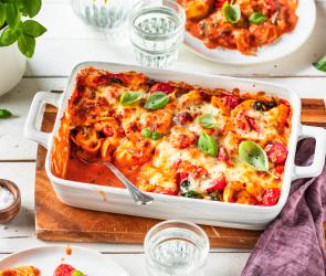 Tortellini Auflauf auf einem gedeckten Tisch in einer weißen Auflaufform.