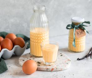 Eierlikör selbst gemacht in einer Glasflasche und Glas, daneben frische Eier.