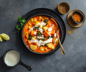 Kartoffelcurry mit Kokosnuss und Kräutern in einer dunklen Schale.