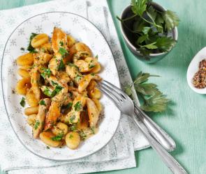 Ein Teller mit Gnocchi und Hähnchen mit Petersilie und Sauce garniert.