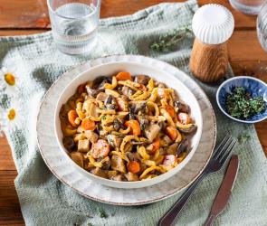 Spätzle mit Pilzragout in einem tiefen, weißen Teller auf einem Tuch.