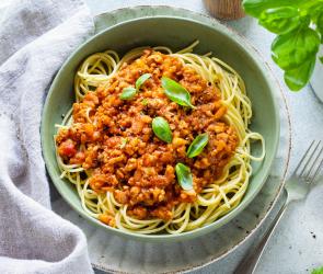 Vegane Bolognese mit Spaghetti in einem hellgrünen tiefen Teller.