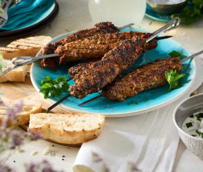 Adana Kebap (Türkische Hackfleischspieße) auf Metallspießen auf einem türkisen Teller.