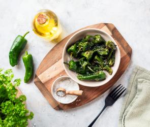 Pimientos de Padron in einer Schüssel auf einem Holzbrett.