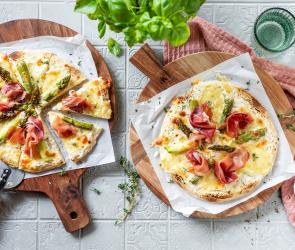 Spargel Pizza bianca mit Schinken und Mozzarella auf zwei Holzbrettern.