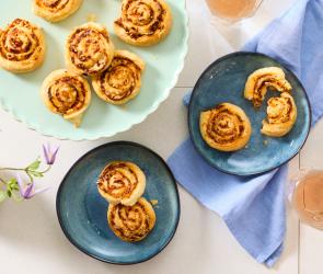 Schnelle Pizzaschnecken aus Blätterteig auf bunten Tellern.
