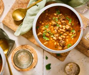 Bohneneintopf mit Rind (Kuru Fasulye) in einem Suppenteler mit goldfarbenem Löffel.