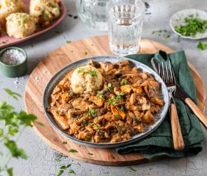 Schwammerlgulasch mit gemischten Pilzen und Klößenauf Tellern.