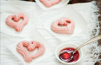 Mehrere Baiserherzen mit Himbeersirup auf einem Tuch.