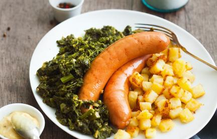 Grünkohl mit Wurst und Röstkartoffelwürfeln auf einem Teller angerichtet.
