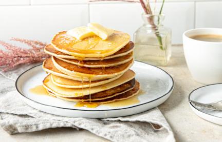 Pancakes amerikanisch übereinander gestapelt mit Butter und Sirup auf einem Teller.